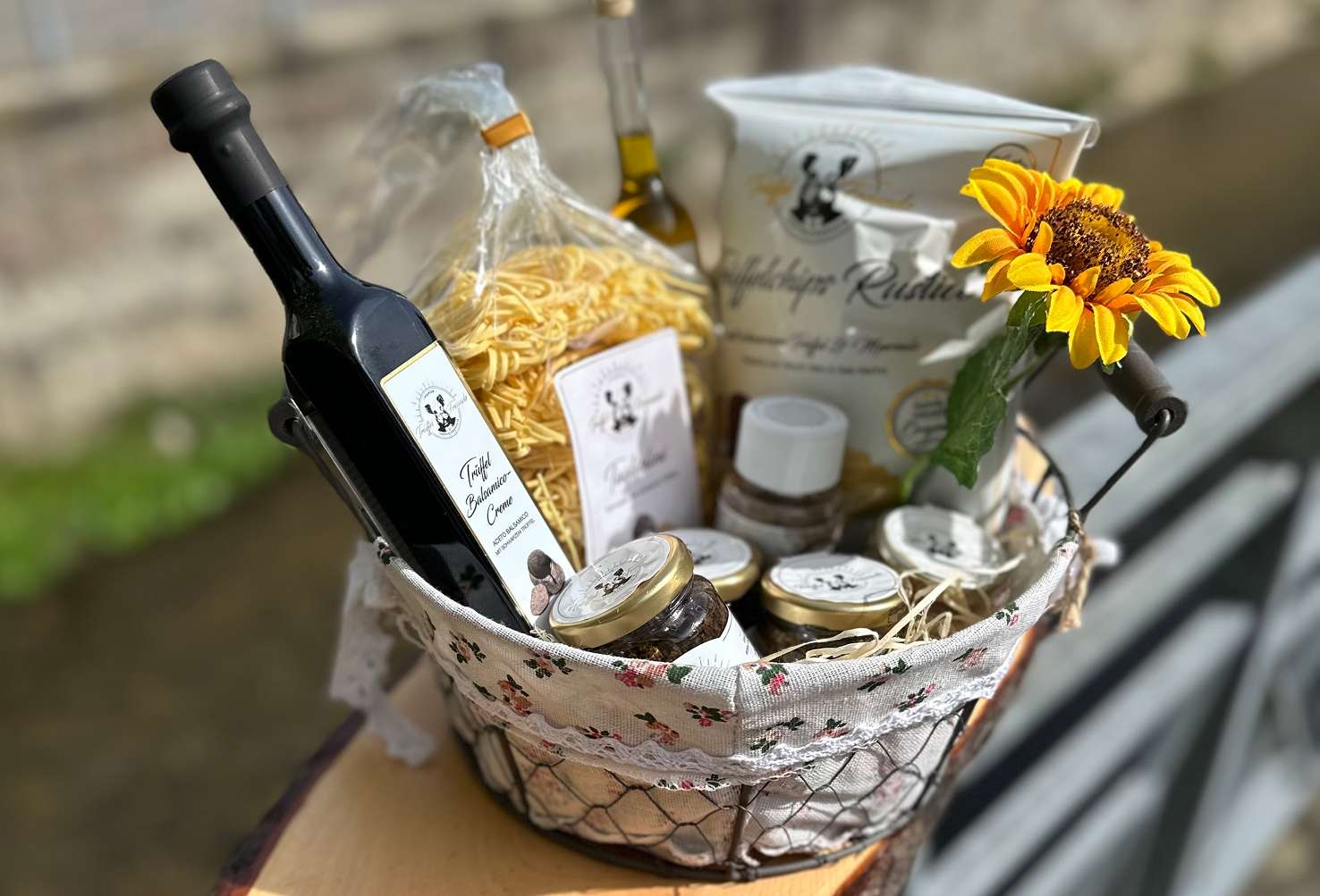 Feinkost-Geschenkkorb mit Pasta, einer Flasche und Gläsern, dekoriert mit gelben Blüten