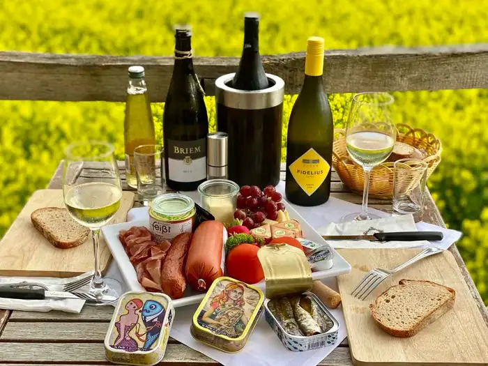 Gedeckter Tisch im Freien mit Sardinendosen, Wein, Brot, Käse und Gemüse